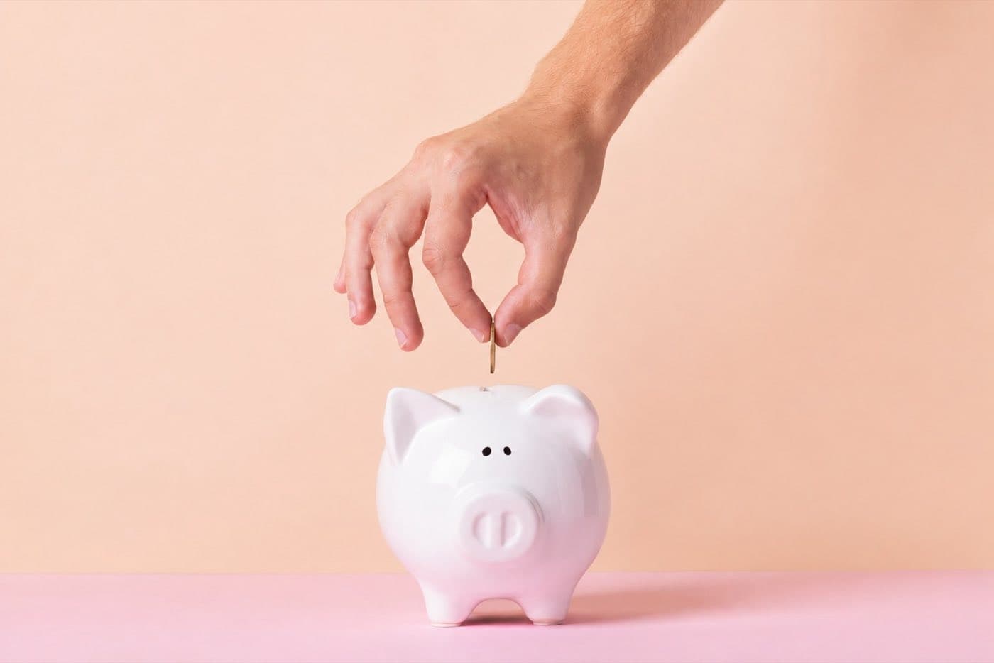 Hand wirft eine Münze in ein Sparschwein